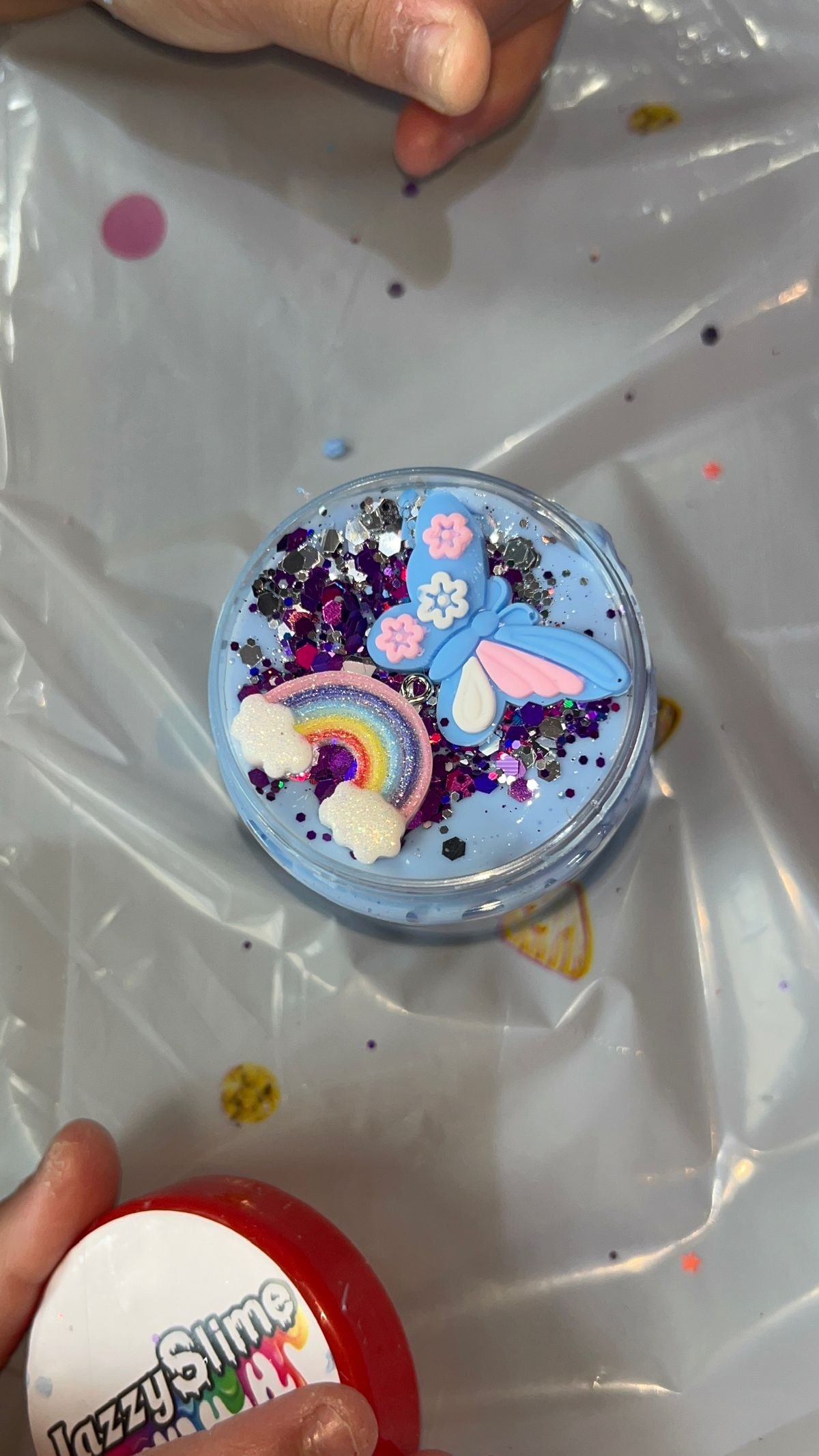 A hand holding a rainbow-decorated Jazzy Slime pot