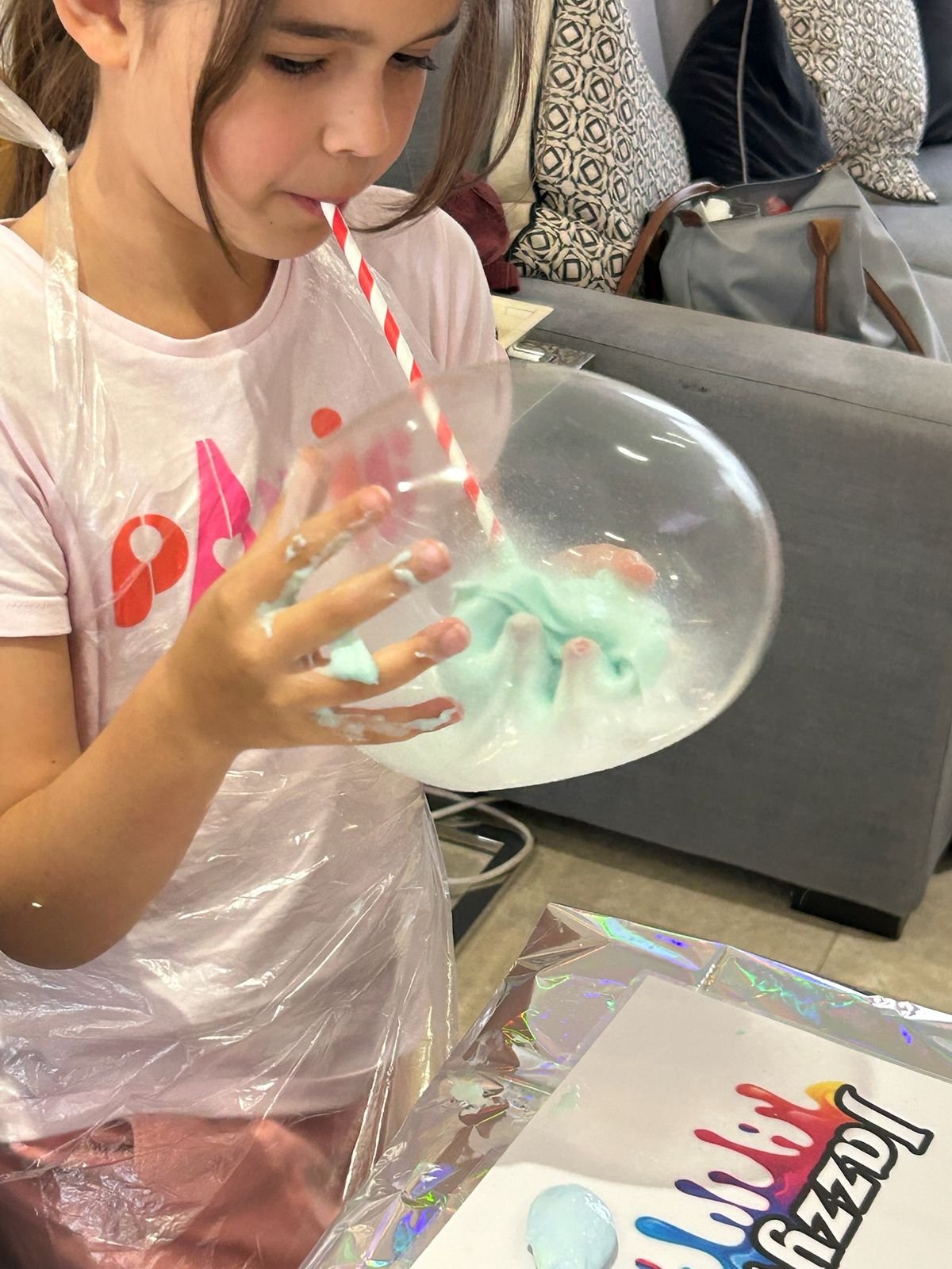 A child blowing a giant slime bubble through a straw
