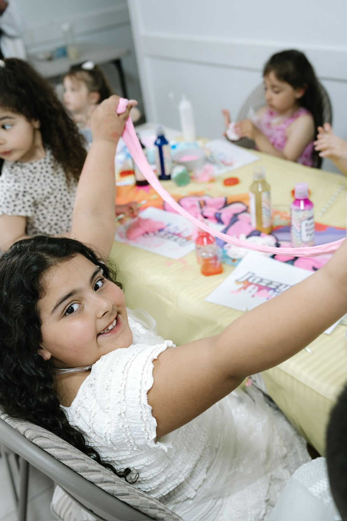 Girls joyfully raising a stretched slime rope at a party